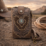 Brown leather phone case with intricate designs on a dirt surface with a cowboy hat and lasso in the background.